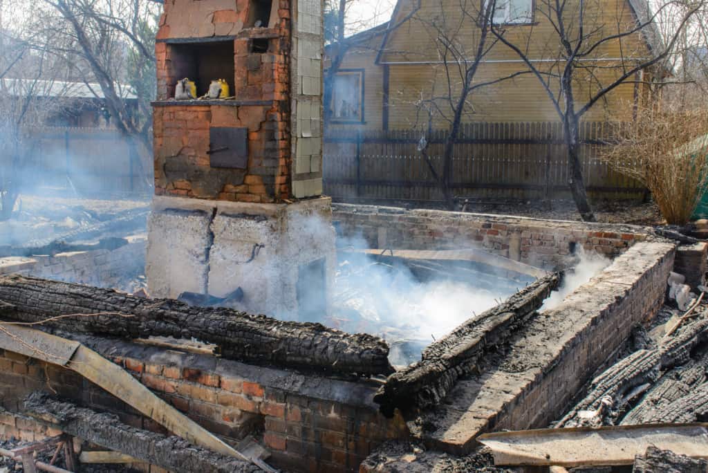 A smoldering aftermath: charred remains of a wooden structure with only a brick chimney left standing.